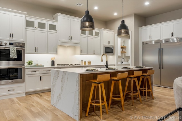 4708 S Sequoia Ave, Broken Arrow, OK 74011 - kitchen featuring built in appliances, light wood-style flooring, recessed lighting, a kitchen island with sink, and a breakfast bar