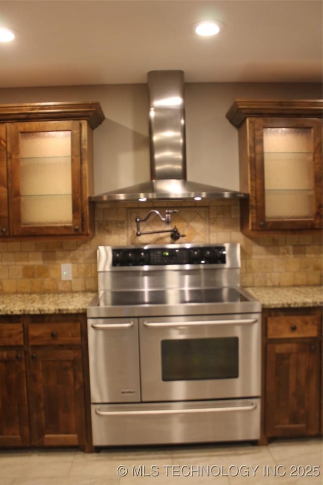 2148 E Wise Rd, Mcalester, OK 74501 - kitchen with stainless steel electric stove, wall chimney exhaust hood, backsplash, glass insert cabinets, and light stone countertops
