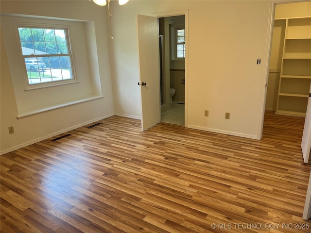 1918 E 14th, Ada, OK 74820 - unfurnished bedroom with a walk in closet, wood finished floors, connected bathroom, and a closet
