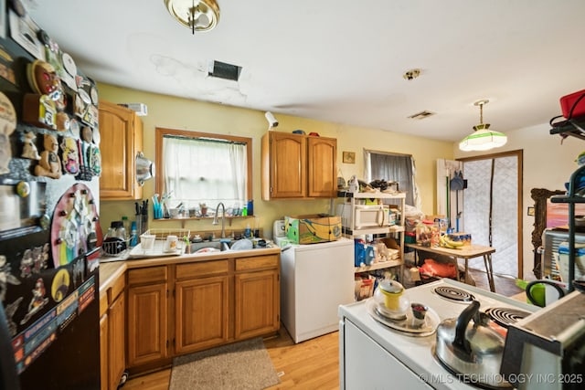 1012 N Irvington St, Tulsa, OK 74115 - kitchen with light countertops, light wood-style floors, brown cabinets, decorative light fixtures, and washer and clothes dryer