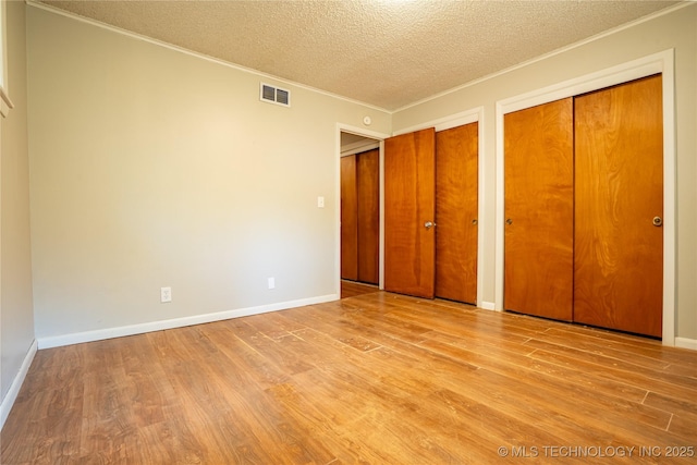 6781 E 26th Pl, Tulsa, OK 74129 - unfurnished bedroom with ornamental molding, a textured ceiling, wood finished floors, and two closets