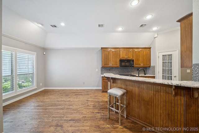 4205 N Narcissus Ave, Broken Arrow, OK 74012 - kitchen with black microwave, a breakfast bar area, lofted ceiling, backsplash, and brown cabinetry