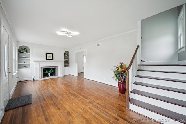 1601 E 6th St, Okmulgee, OK 74447 - unfurnished living room featuring wood finished floors, built in features, stairs, and a brick fireplace