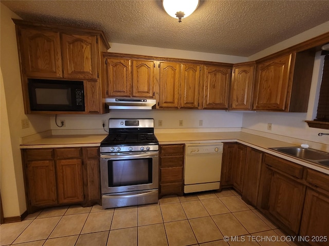 428101 E 1150th Rd, Porum, OK 74455 - kitchen featuring black microwave, stainless steel gas range oven, white dishwasher, under cabinet range hood, and brown cabinets