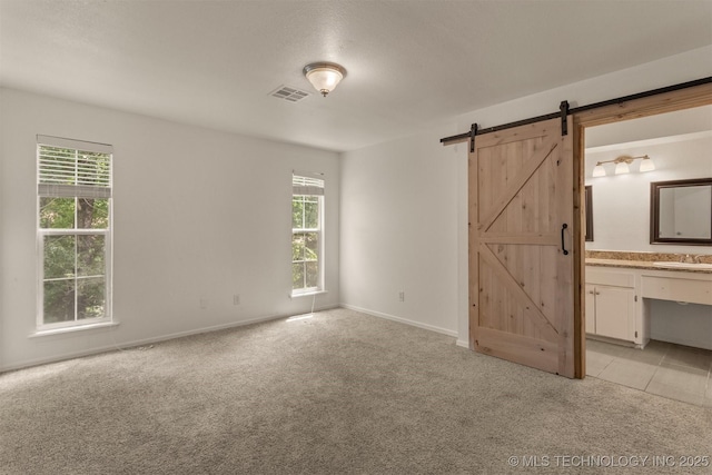 5117 S Lions Ave, Broken Arrow, OK 74011 - unfurnished bedroom with a barn door, multiple windows, light carpet, and ensuite bath