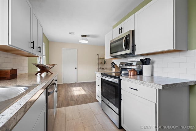 321 NE Elmhurst Ave, Bartlesville, OK 74006 - kitchen featuring stainless steel appliances, backsplash, white cabinets, light countertops, and light wood-style flooring