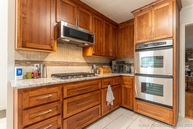 3107 E 84th St, Tulsa, OK 74137 - kitchen featuring appliances with stainless steel finishes, decorative backsplash, brown cabinetry, and light stone countertops
