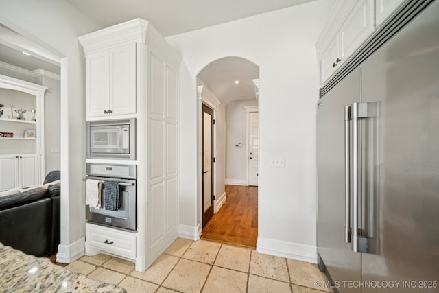 905 W Elmira St, Broken Arrow, OK 74012 - kitchen featuring built in appliances, arched walkways, white cabinets, stone tile flooring, and crown molding