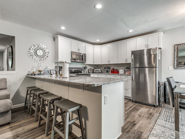 4640 E 68th St Unit 285, Tulsa, OK 74136 - kitchen with appliances with stainless steel finishes, a peninsula, wood finished floors, a breakfast bar, and a textured ceiling