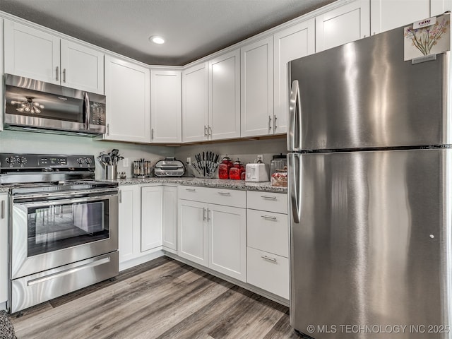 4640 E 68th St Unit 285, Tulsa, OK 74136 - kitchen featuring appliances with stainless steel finishes, white cabinets, wood finished floors, recessed lighting, and light stone countertops