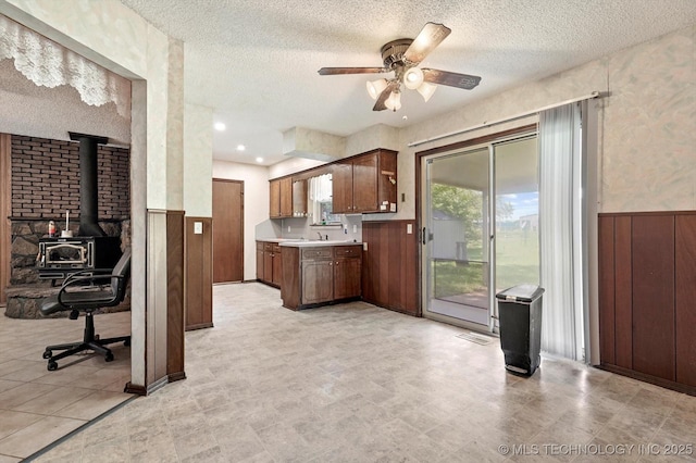 16429 E 1st St, Tulsa, OK 74108 - kitchen featuring a wainscoted wall, ceiling fan, a textured ceiling, light countertops, and a wood stove