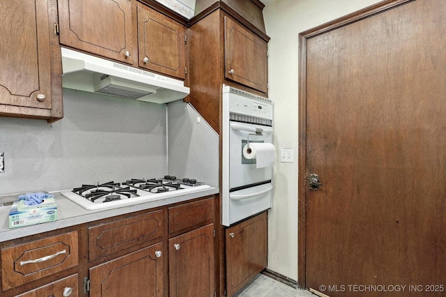 16429 E 1st St, Tulsa, OK 74108 - kitchen featuring under cabinet range hood, white appliances, a warming drawer, light countertops, and brown cabinets