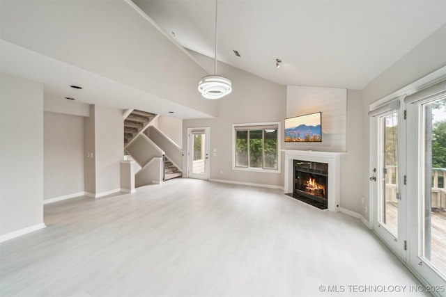 5743 E 72nd Pl Unit 11, Tulsa, OK 74136 - unfurnished living room featuring a fireplace with flush hearth, light wood-style floors, stairs, and high vaulted ceiling