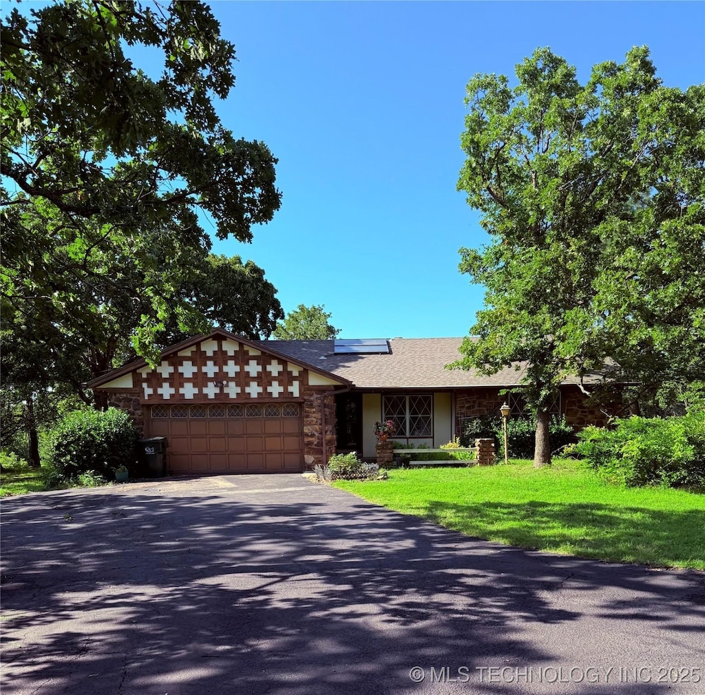 28265 Forest Ridge Rd, Sand Springs, OK 74063 - view of front facade featuring asphalt driveway, an attached garage, roof mounted solar panels, stone siding, and a front lawn