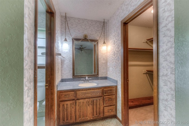 28265 Forest Ridge Rd, Sand Springs, OK 74063 - bathroom with a textured ceiling, a spacious closet, vanity, wallpapered walls, and a ceiling fan
