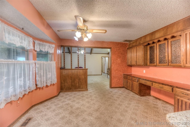 28265 Forest Ridge Rd, Sand Springs, OK 74063 - kitchen with brown cabinetry, built in desk, light colored carpet, a ceiling fan, and a textured ceiling