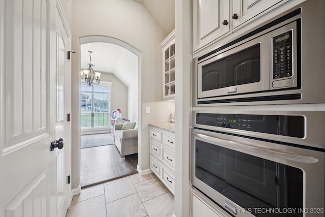 5814 130th W Ave, Sand Springs, OK 74063 - kitchen featuring appliances with stainless steel finishes, lofted ceiling, a chandelier, glass insert cabinets, and arched walkways