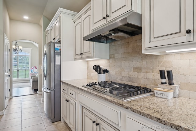 5814 130th W Ave, Sand Springs, OK 74063 - kitchen featuring under cabinet range hood, appliances with stainless steel finishes, arched walkways, backsplash, and light stone countertops