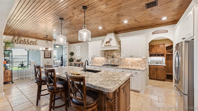 14934 S Sequoia St, Glenpool, OK 74033 - kitchen featuring freestanding refrigerator, custom range hood, stone tile floors, a center island with sink, and wooden ceiling