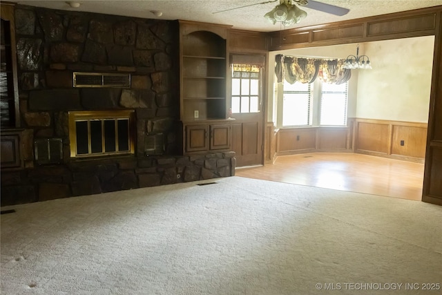204 E 24th Ct, Owasso, OK 74055 - unfurnished living room featuring carpet flooring, a ceiling fan, a wainscoted wall, wood finished floors, and a stone fireplace