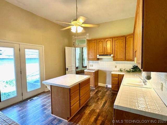 349 S Foreman St, Vinita, OK 74301 - kitchen featuring dark wood-style floors, backsplash, brown cabinetry, ceiling fan, and under cabinet range hood