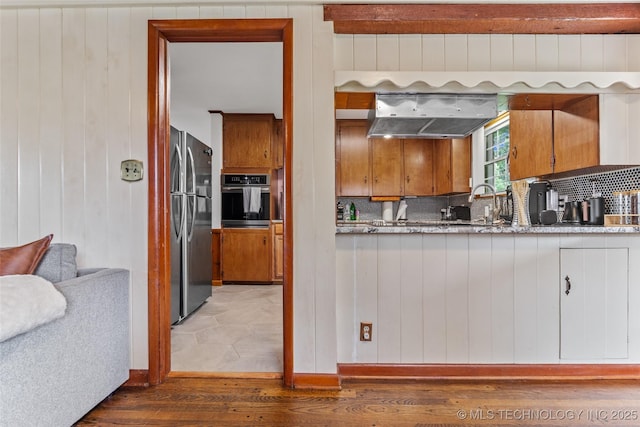 5225 S Toledo Ave, Tulsa, OK 74135 - kitchen featuring stainless steel appliances, light wood-style flooring, tasteful backsplash, under cabinet range hood, and wooden walls