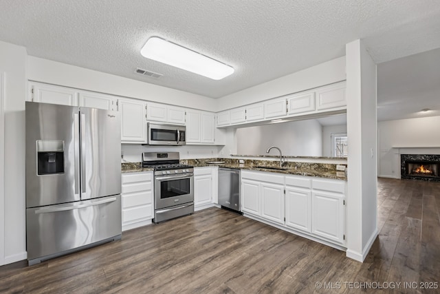 8316 E 81st Pl, Tulsa, OK 74133 - kitchen with appliances with stainless steel finishes, dark wood-style floors, white cabinets, a textured ceiling, and a fireplace