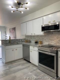 4822 S Quaker Ave, Tulsa, OK 74105 - kitchen with stainless steel appliances, a chandelier, white cabinetry, a peninsula, and backsplash