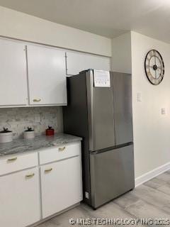 4822 S Quaker Ave, Tulsa, OK 74105 - kitchen with freestanding refrigerator, white cabinets, decorative backsplash, and light stone countertops