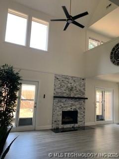 4822 S Quaker Ave, Tulsa, OK 74105 - unfurnished living room featuring a towering ceiling, wood finished floors, a stone fireplace, and a ceiling fan