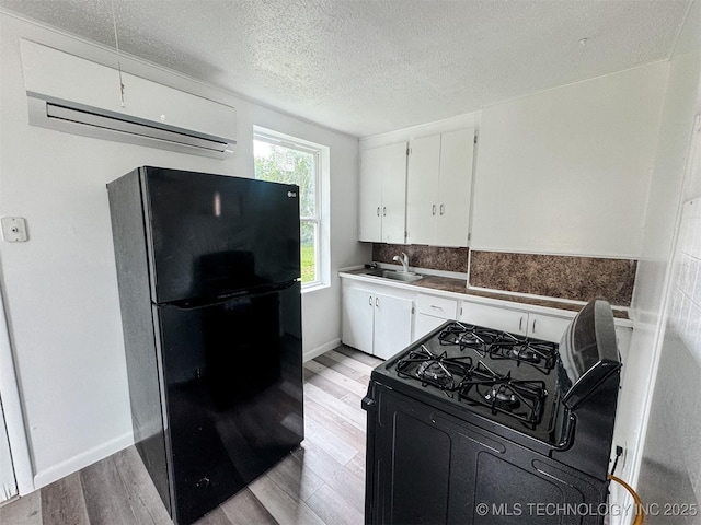 916 Coy Ave, Tahlequah, OK 74464 - kitchen with black appliances, a wall unit AC, light wood-type flooring, white cabinetry, and a textured ceiling
