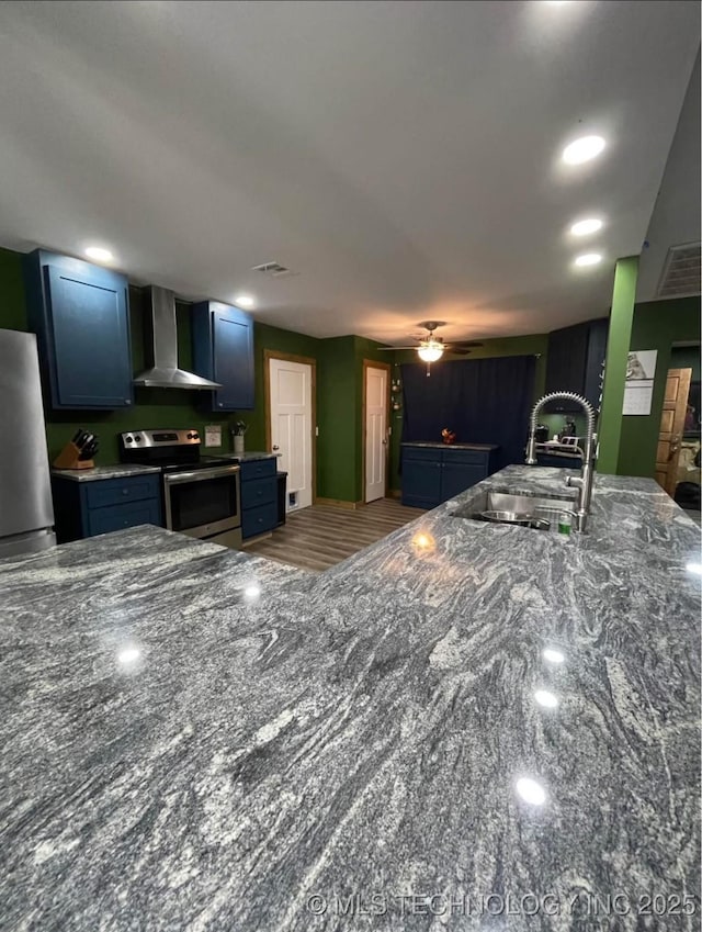 23422 E 79th St S, Broken Arrow, OK 74014 - kitchen with wall chimney exhaust hood, stainless steel appliances, dark stone counters, ceiling fan, and blue cabinets