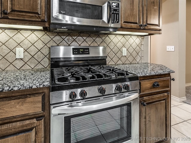 4667 E 144th Pl S, Bixby, OK 74008 - kitchen featuring appliances with stainless steel finishes, light tile patterned flooring, decorative backsplash, light stone countertops, and dark brown cabinetry
