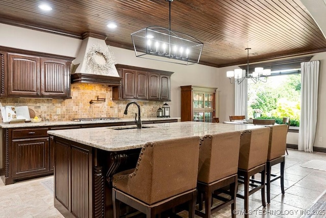 2015 W 109th St, Jenks, OK 74037 - kitchen with a chandelier, premium range hood, wood ceiling, an island with sink, and decorative backsplash