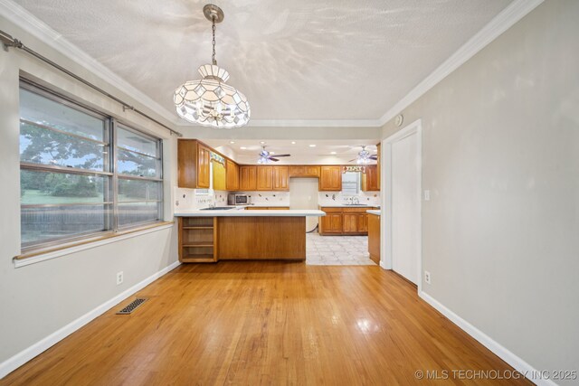3002 E 80th Pl, Tulsa, OK 74136 - kitchen featuring a peninsula, light wood-style floors, brown cabinets, light countertops, and crown molding