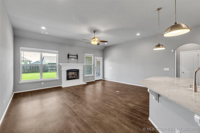 2012 W Huntsville Pl, Broken Arrow, OK 74011 - unfurnished living room featuring ceiling fan, arched walkways, dark wood-style flooring, recessed lighting, and a fireplace with raised hearth