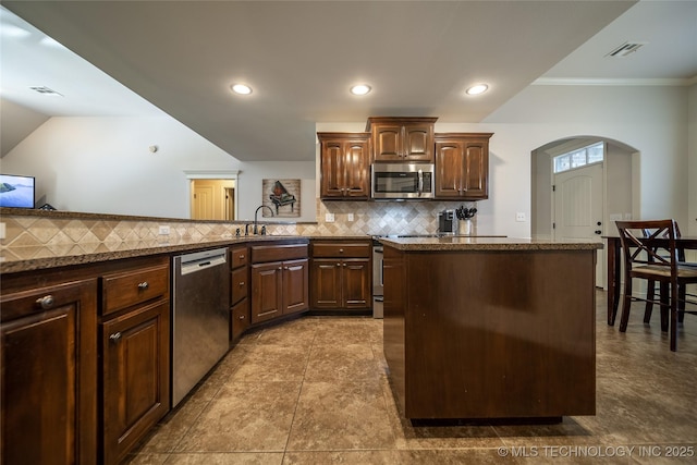 14701 E 150th St, Collinsville, OK 74021 - kitchen with appliances with stainless steel finishes, arched walkways, decorative backsplash, a kitchen island, and recessed lighting