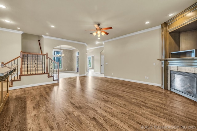 14651 S Gary Ave, Bixby, OK 74008 - unfurnished living room featuring ceiling fan, a tiled fireplace, crown molding, arched walkways, and wood finished floors