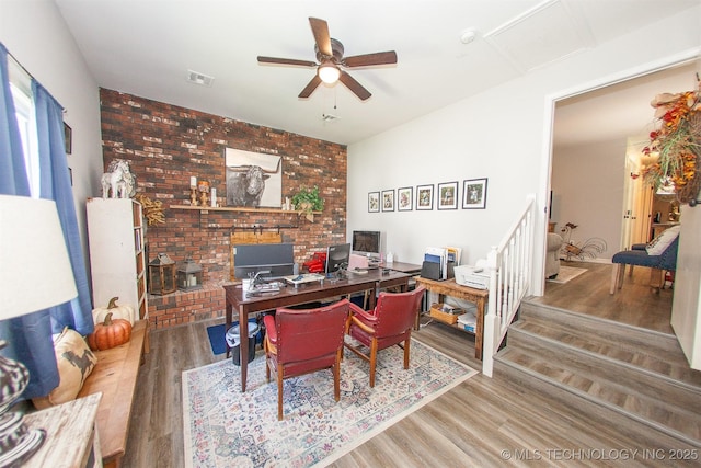 1119 N Oklahoma Ave, Claremore, OK 74017 - home office with a ceiling fan, wood finished floors, brick wall, and a wood stove