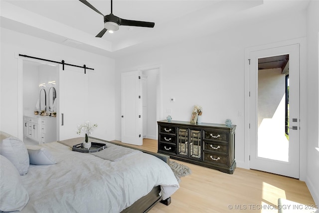 12005 S Vandalia Ave, Tulsa, OK 74137 - bedroom with a barn door, light wood-type flooring, a tray ceiling, and ceiling fan