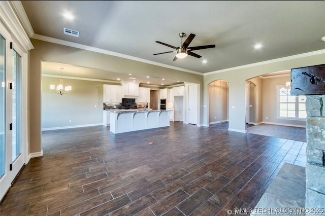 9022 N 65th Pl E, Owasso, OK 74055 - unfurnished living room with ceiling fan, arched walkways, a chandelier, dark wood-type flooring, and ornamental molding