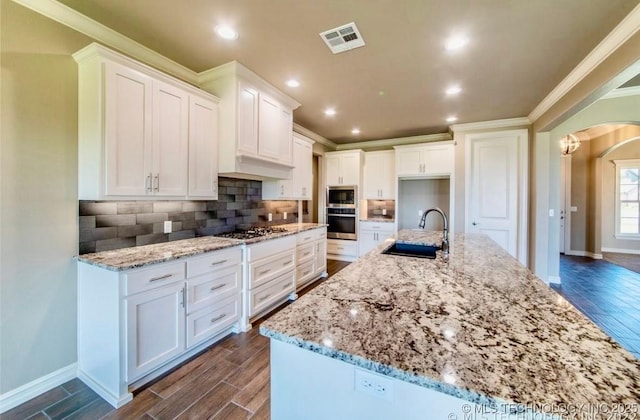 9022 N 65th Pl E, Owasso, OK 74055 - kitchen featuring stainless steel appliances, dark wood finished floors, arched walkways, white cabinets, and crown molding