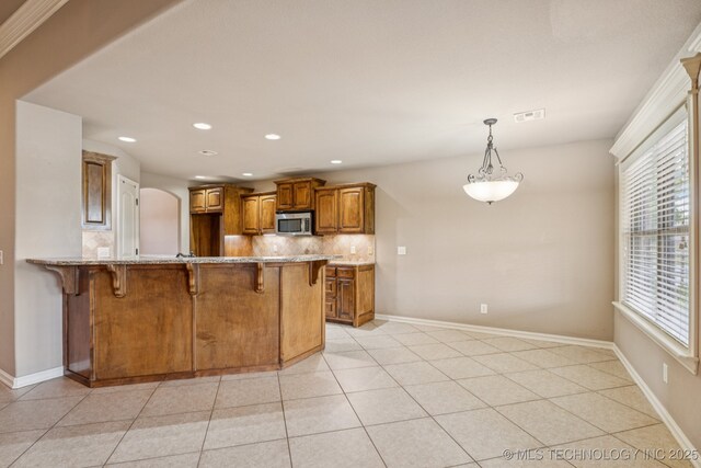 9200 E 92nd Pl, Owasso, OK 74055 - kitchen with stainless steel microwave, a breakfast bar area, brown cabinetry, decorative backsplash, and a peninsula