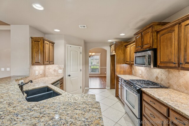 9200 E 92nd Pl, Owasso, OK 74055 - kitchen with appliances with stainless steel finishes, arched walkways, light stone countertops, light tile patterned floors, and tasteful backsplash