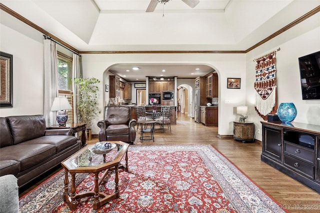 9632 S Vandalia Ave, Tulsa, OK 74137 - living room with arched walkways, a raised ceiling, a ceiling fan, light wood-style flooring, and ornamental molding