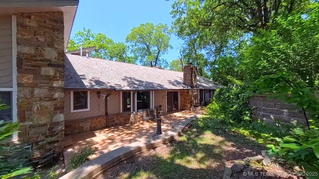 3334 E 100th Pl, Tulsa, OK 74137 - view of front of house with stone siding, a chimney, a patio area, and a shingled roof