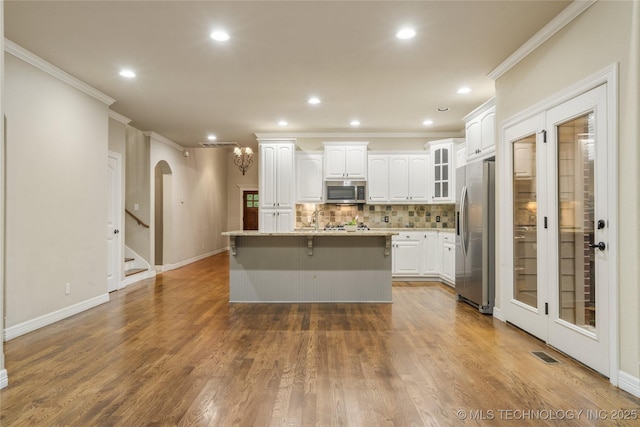 9722 S 75th E Ave, Tulsa, OK 74133 - kitchen featuring appliances with stainless steel finishes, crown molding, white cabinetry, decorative backsplash, and a kitchen island with sink
