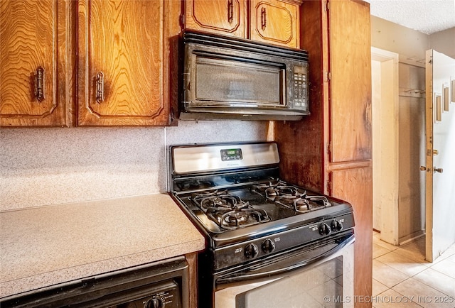 5677 W 3rd St, Tulsa, OK 74127 - kitchen with stainless steel gas range oven, black microwave, light countertops, brown cabinetry, and light tile patterned flooring