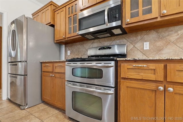 2110 S Javine Ct, Skiatook, OK 74070 - kitchen featuring appliances with stainless steel finishes, brown cabinets, backsplash, and light tile patterned flooring
