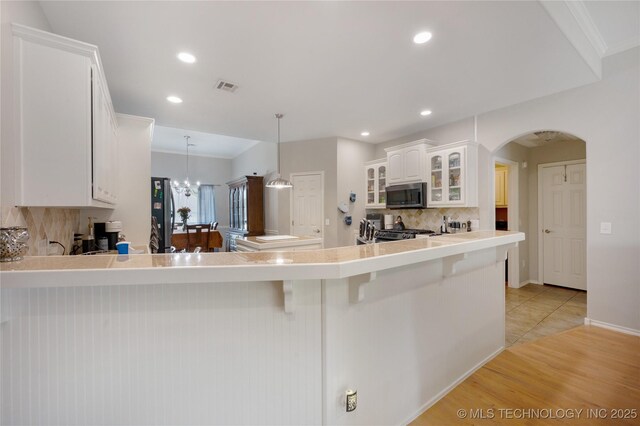 14220 S Vandalia Ave, Bixby, OK 74008 - kitchen featuring appliances with stainless steel finishes, tasteful backsplash, a kitchen breakfast bar, arched walkways, and glass insert cabinets